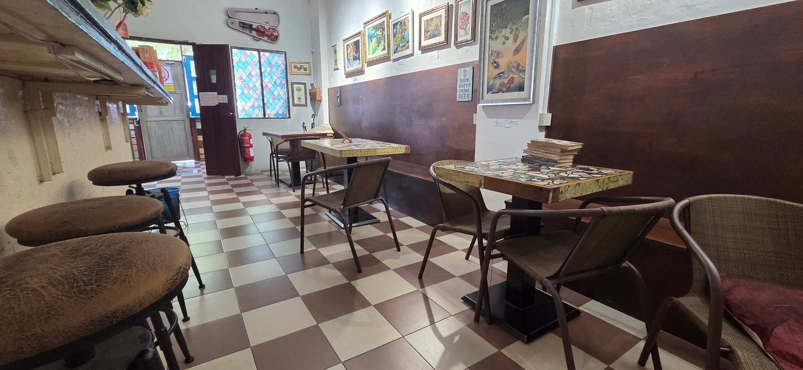 Tables and chairs on a checkered tiled floor inside Sojourn Beds & Cafe, Taiping